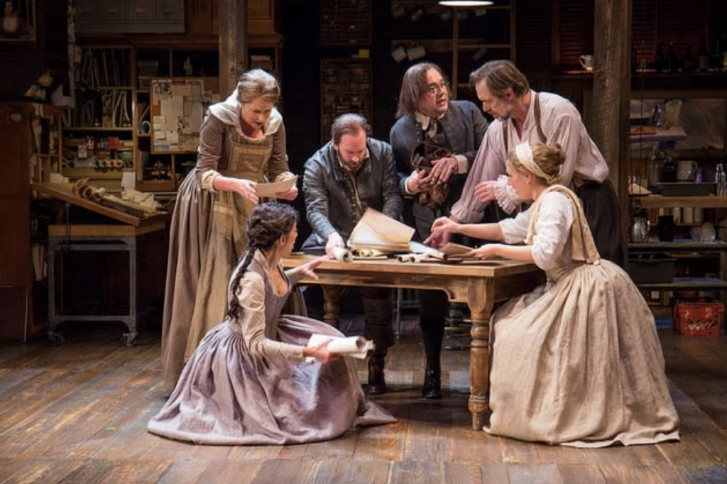 A group of 6 caucasian adults in period clothing on a stage